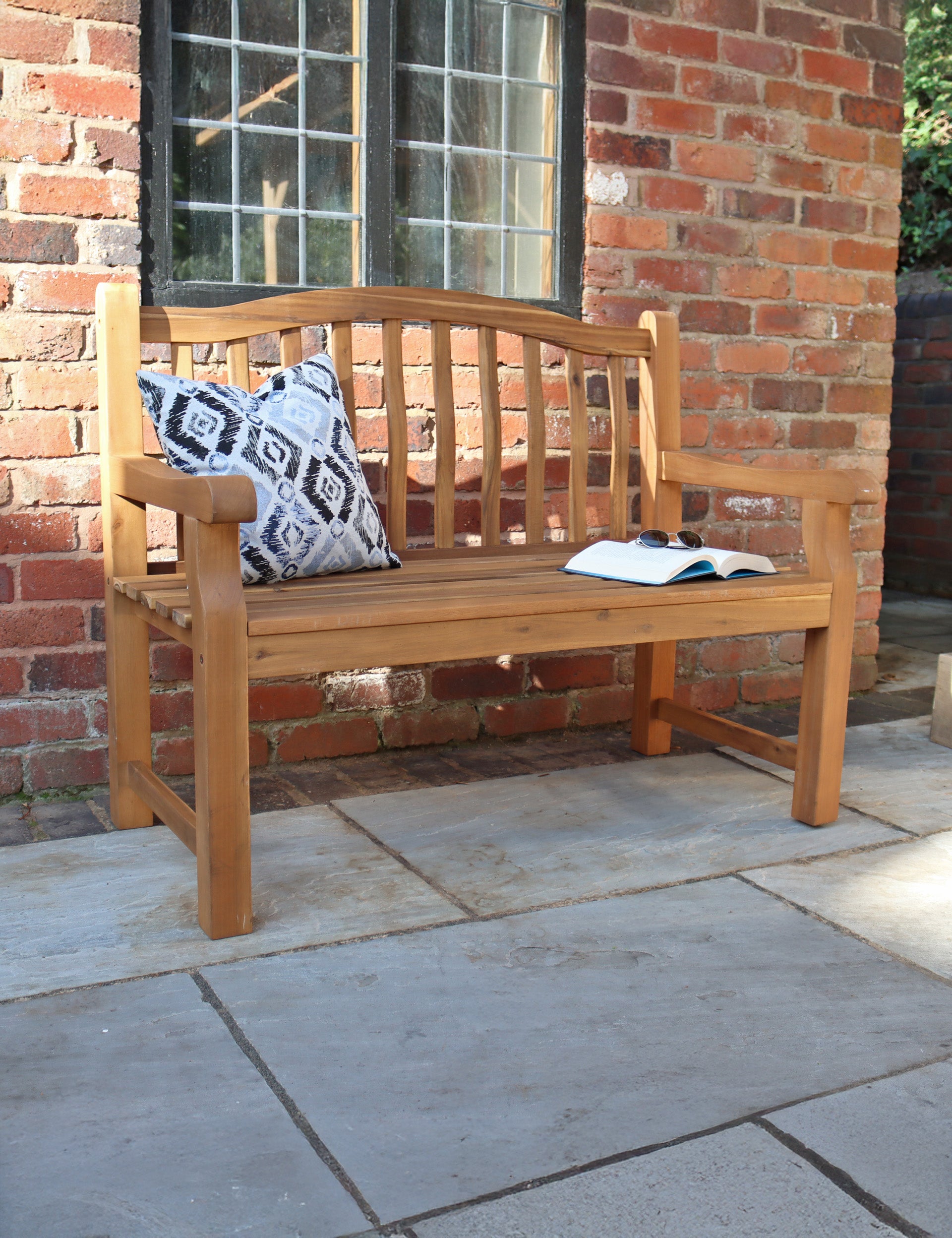 Wooden 2-seater garden bench with cushions and book on patio