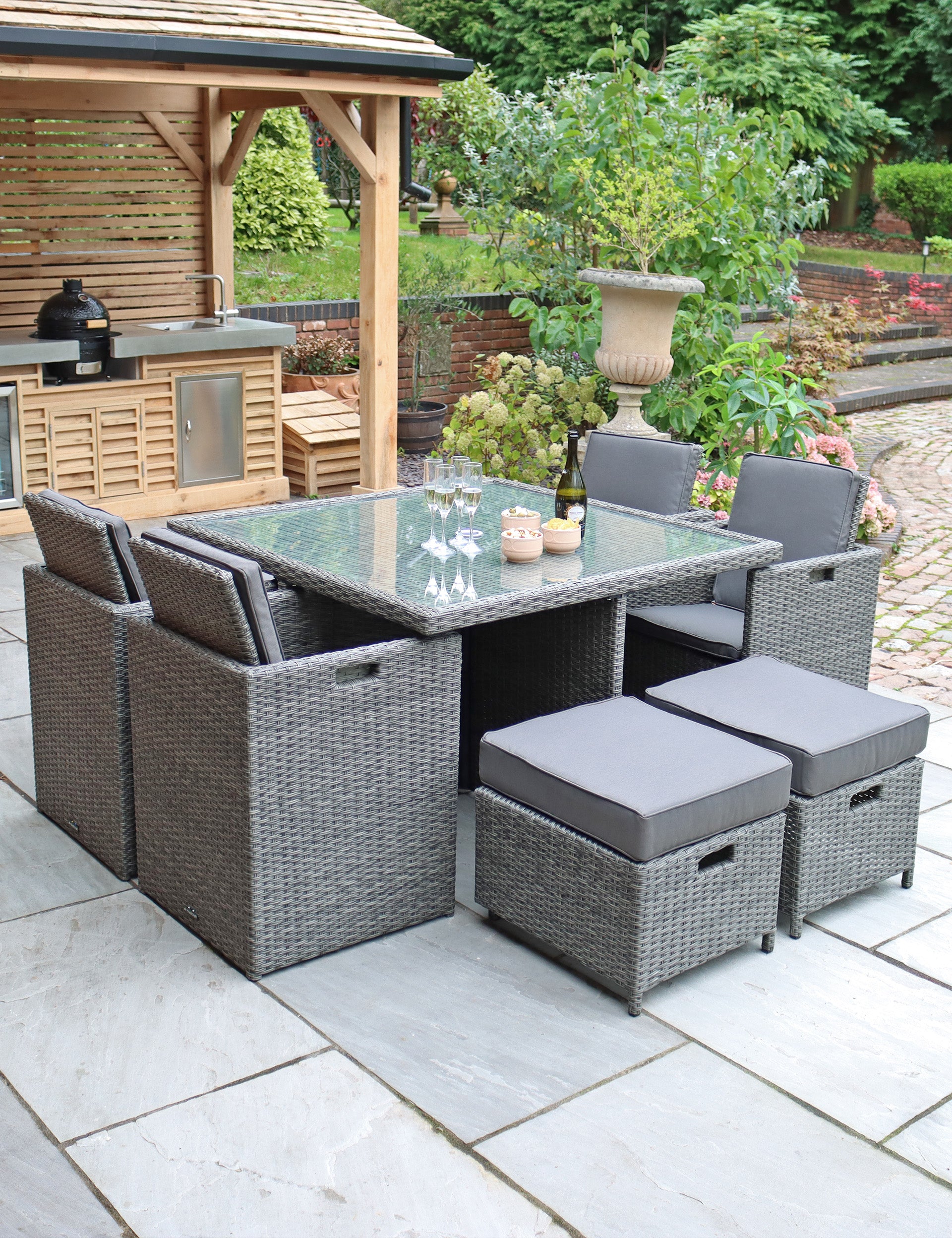 Grey rattan cube outdoor dining set with chairs and stools around glass table