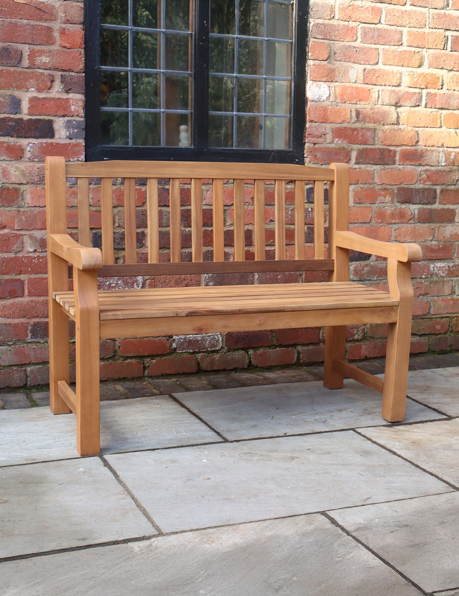Wooden outdoor bench with slatted backrest on a stone patio