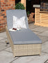 Rattan sun lounger with grey cushion and pillow on a stone patio