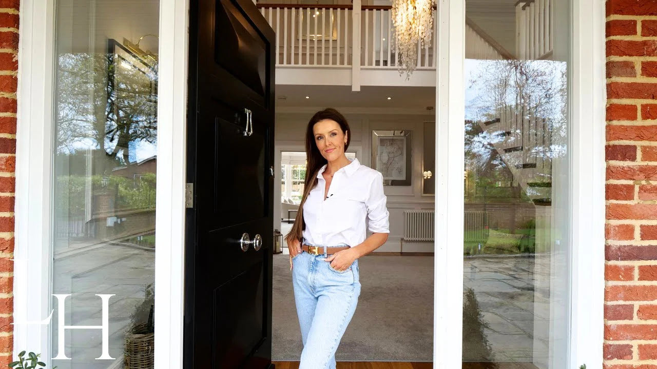 A woman in a white shirt and jeans stands at the doorway of a modern home