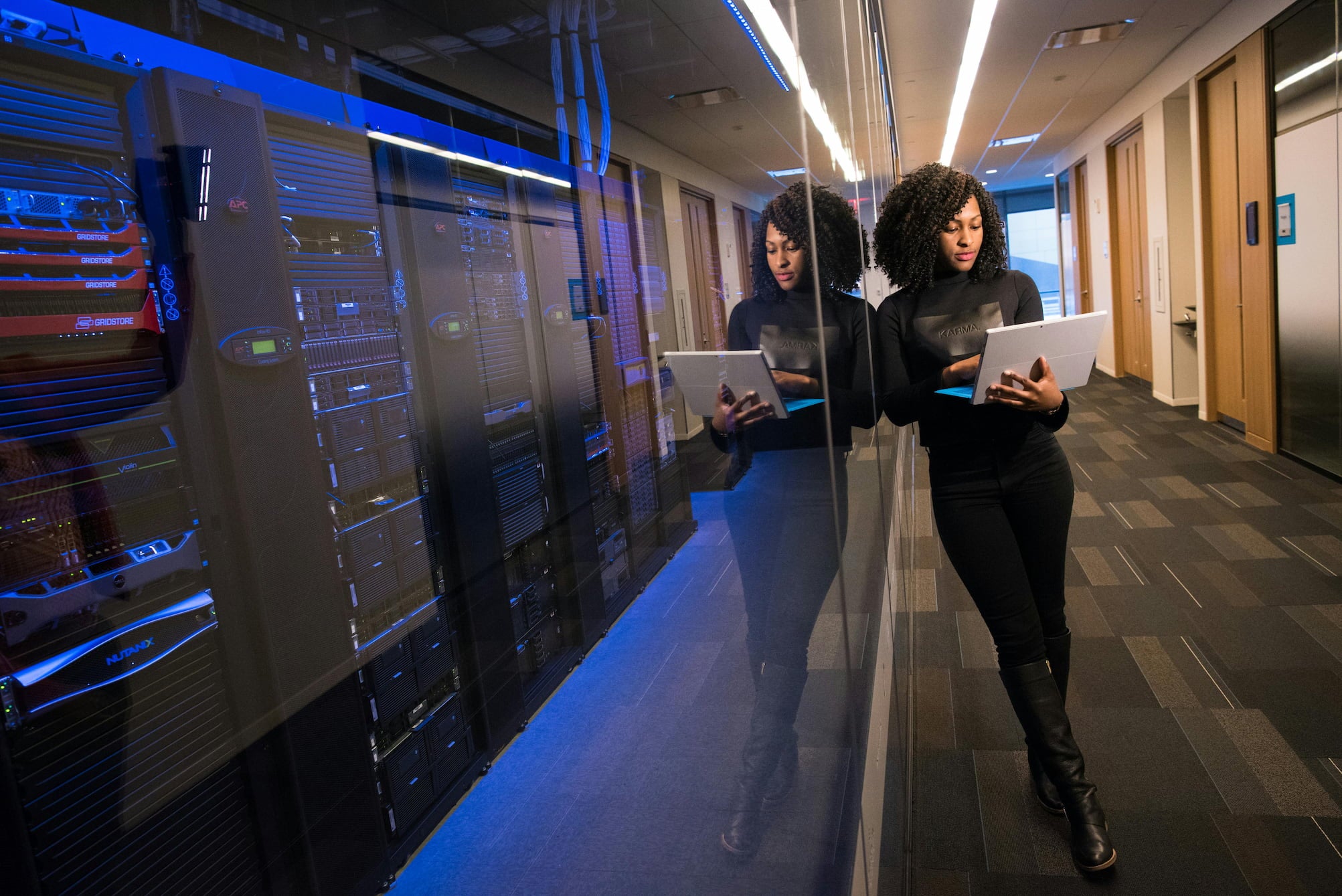 Woman standing in a server room hallway working on a laptop