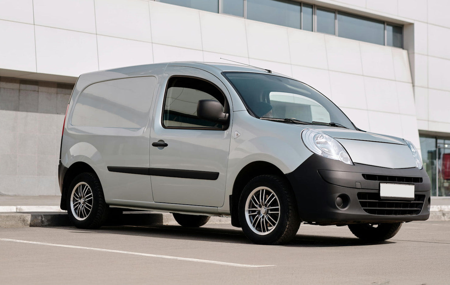 Silver delivery van parked outside a modern building with large windows