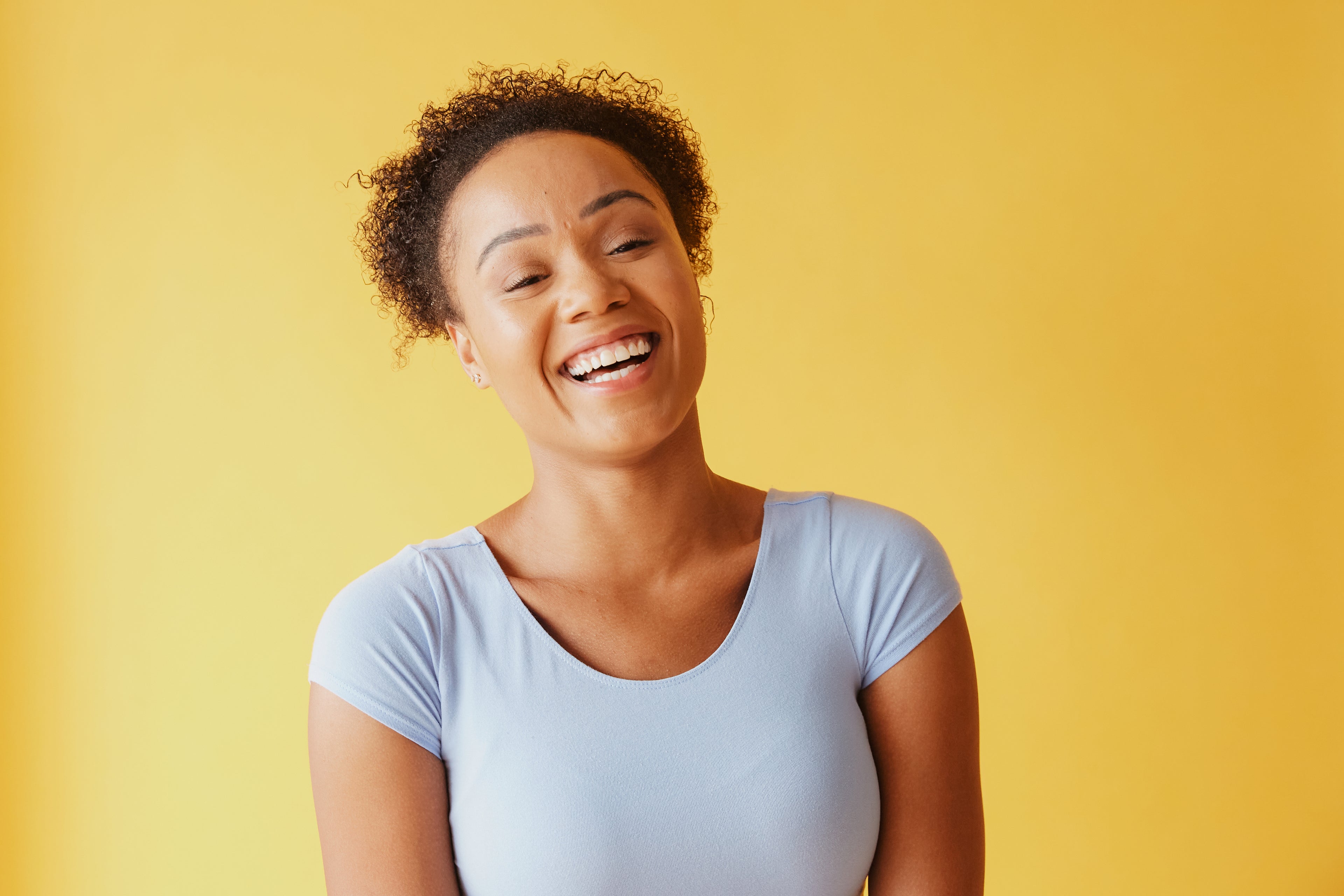 Young woman smiling brightly, wearing casual top, standing against neutral background