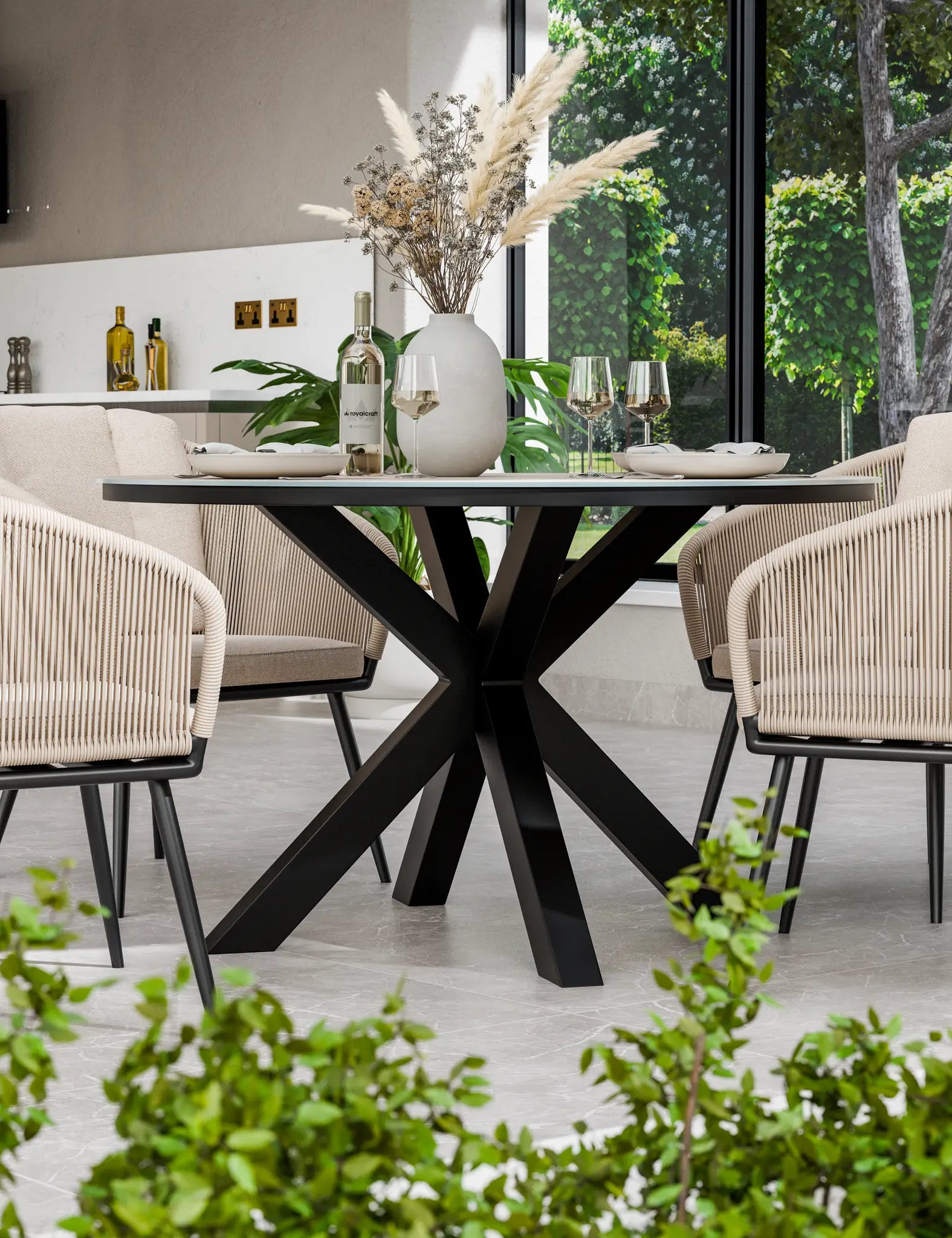Image of Round dining table with black cross-leg base and four rope-woven armchairs with beige cushions