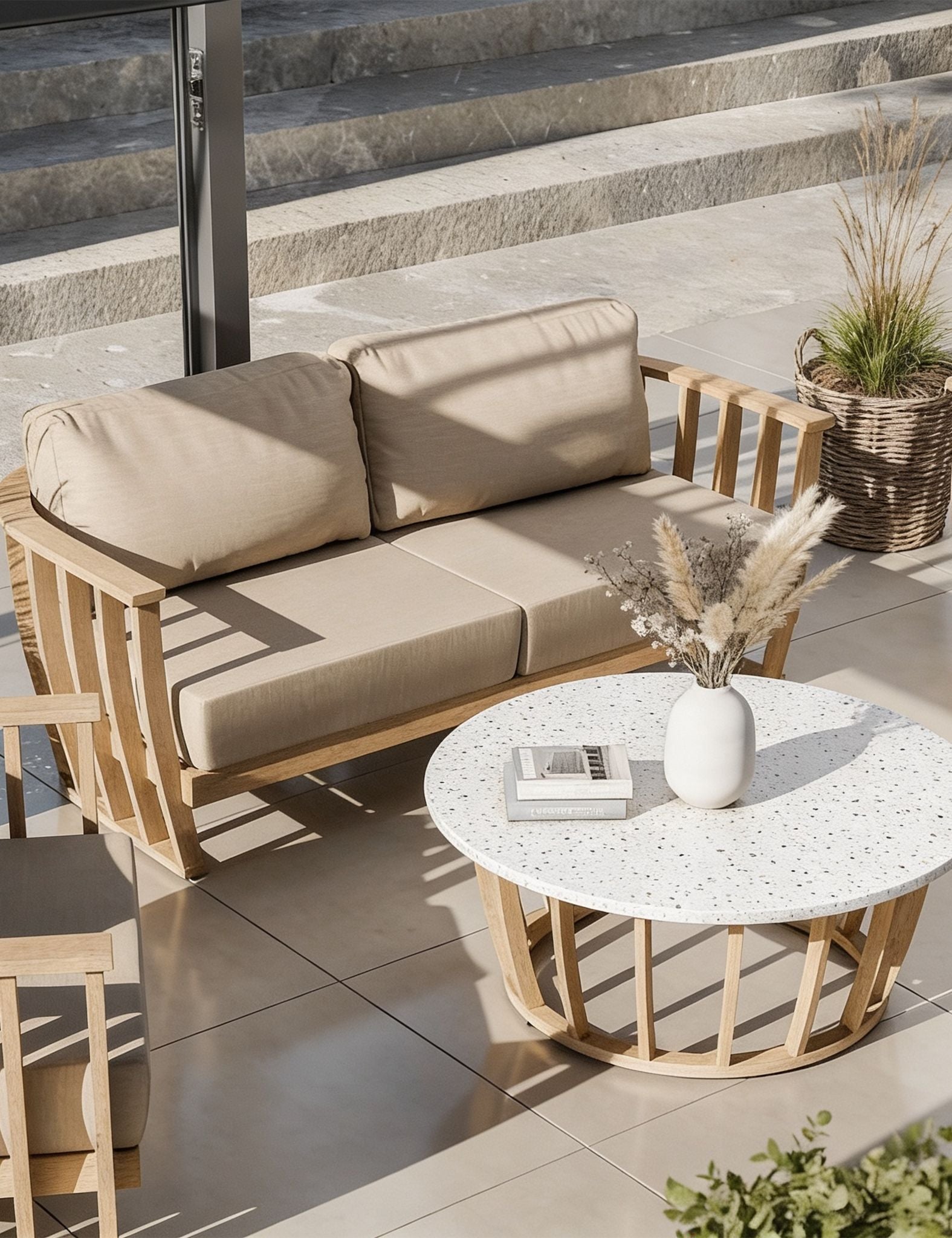 Image of Outdoor patio furniture set featuring a two-seater sofa with beige cushions and a light wood frame, paired with a round white speckled coffee table and a matching wooden side chair on a tiled patio.
