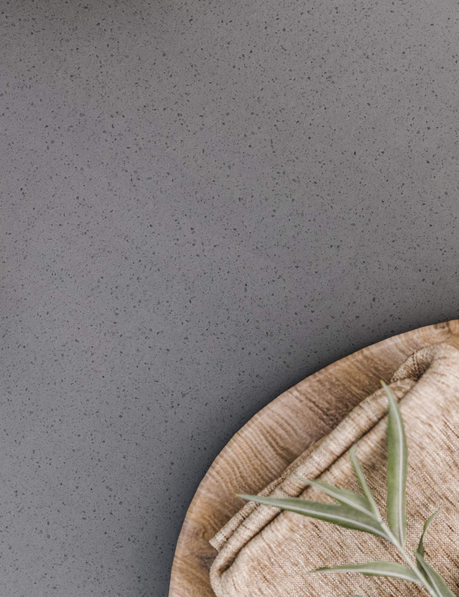 Close-up of grey speckled tabletop with wooden plate, napkin, and green leaf