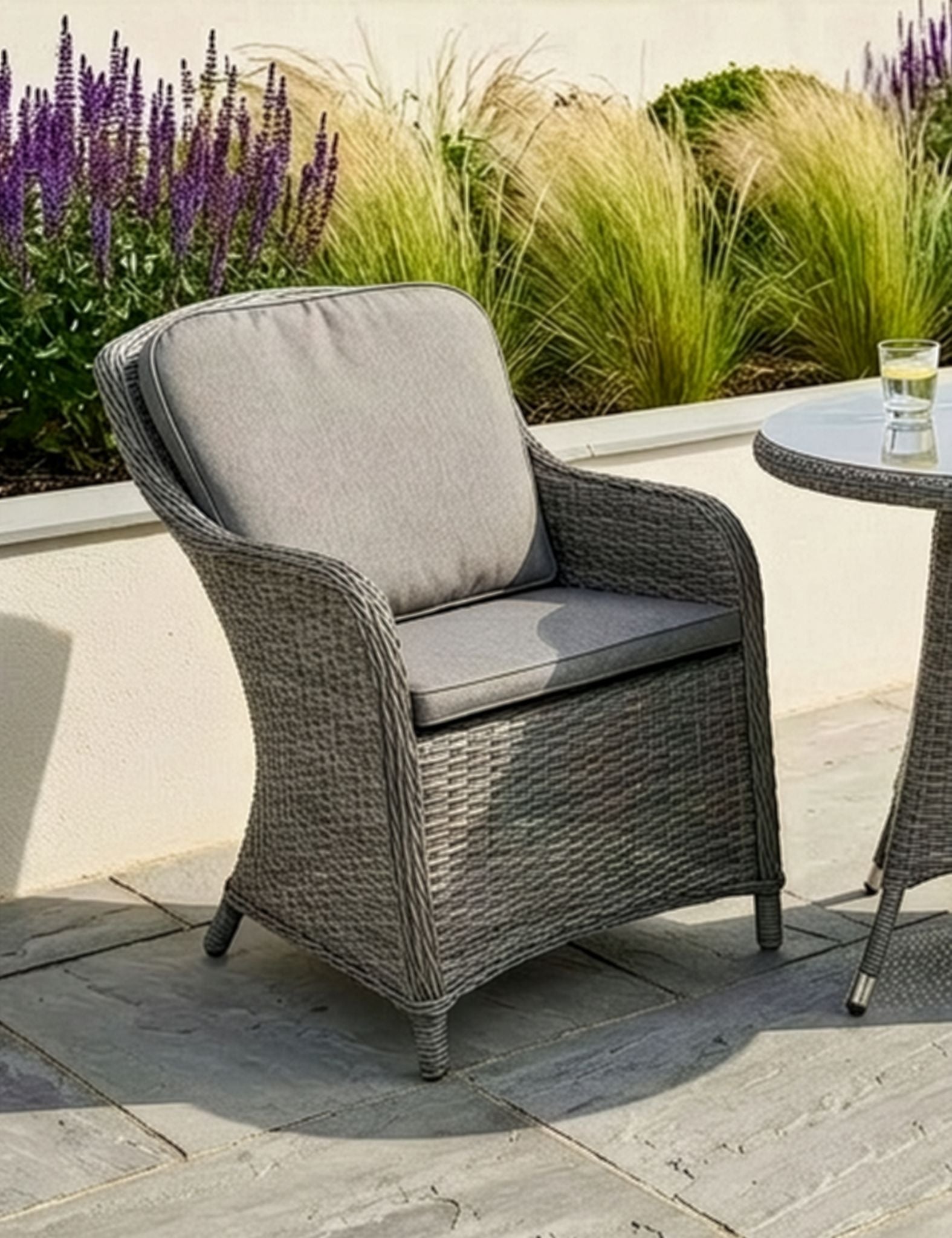 Image of Grey wicker chair with a cushion on a patio with plants in the background