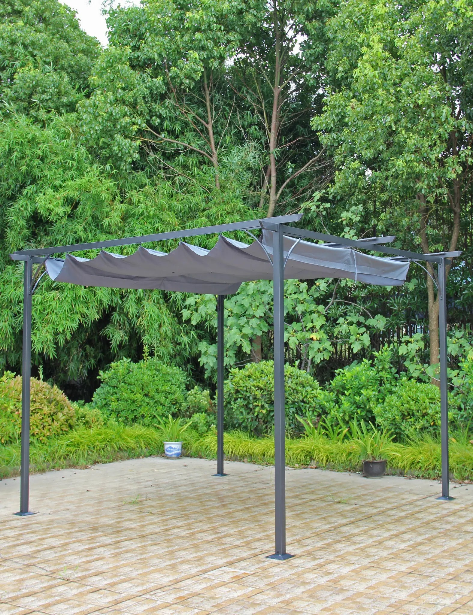 Image of Black metal pergola with canopy set on a paved patio near greenery