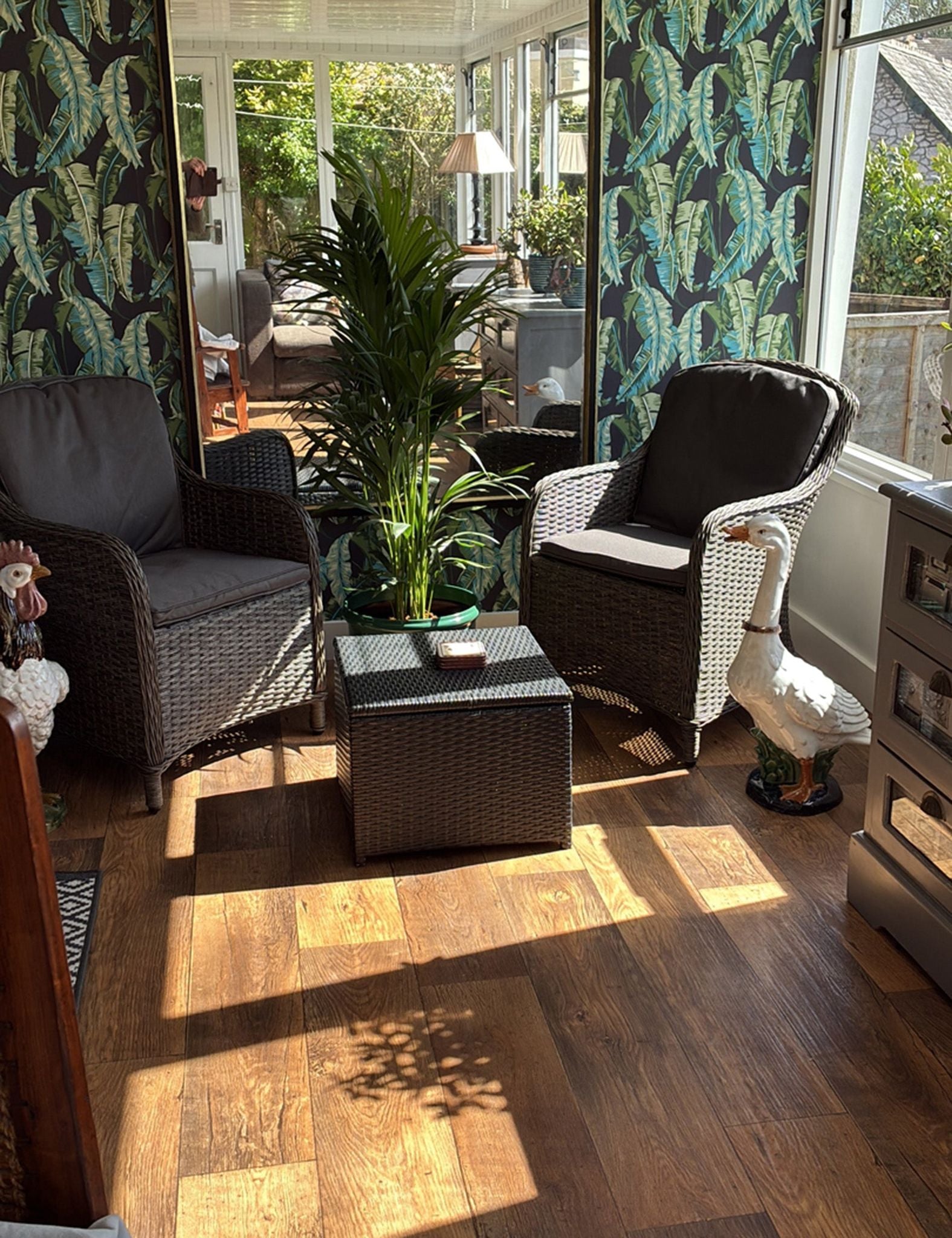 Image of Sunroom with Rattan furniture, plants, and a goose on a wooden floor.