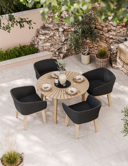 Round wooden patio table with four black cushioned chairs and tableware