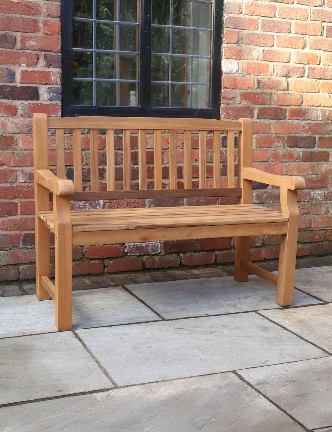 Wooden outdoor bench with slatted backrest on a stone patio