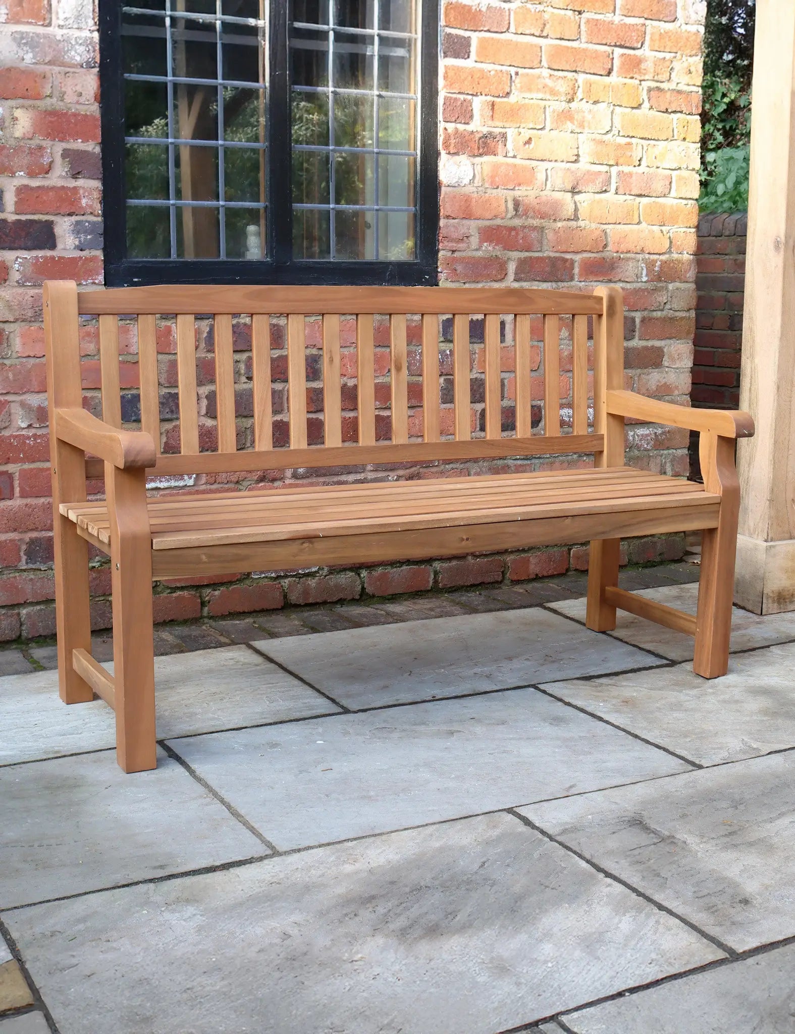 Wooden outdoor bench with slatted backrest on a stone patio