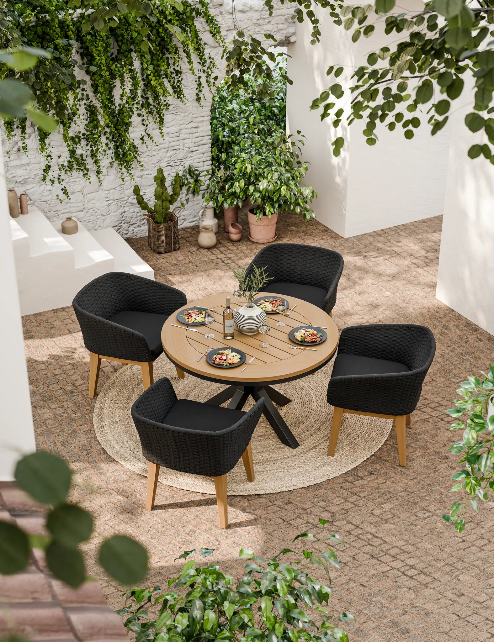 Round wooden dining table with four black cushioned chairs outdoors