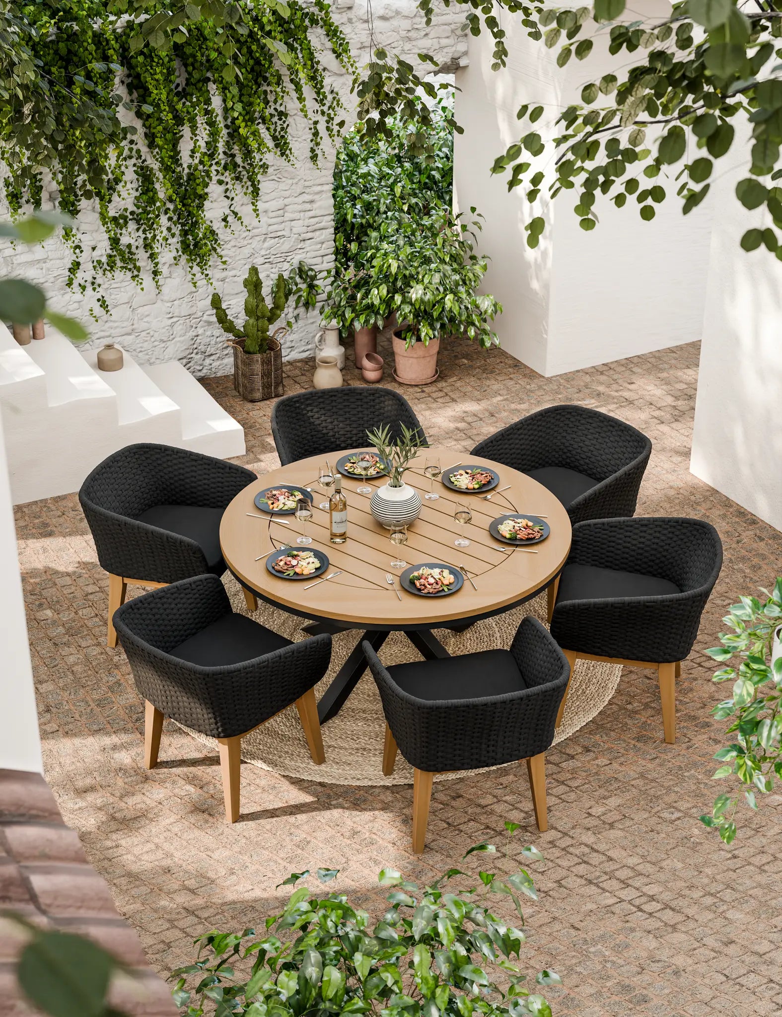 Image of Round wooden dining table with six black cushioned chairs outdoors