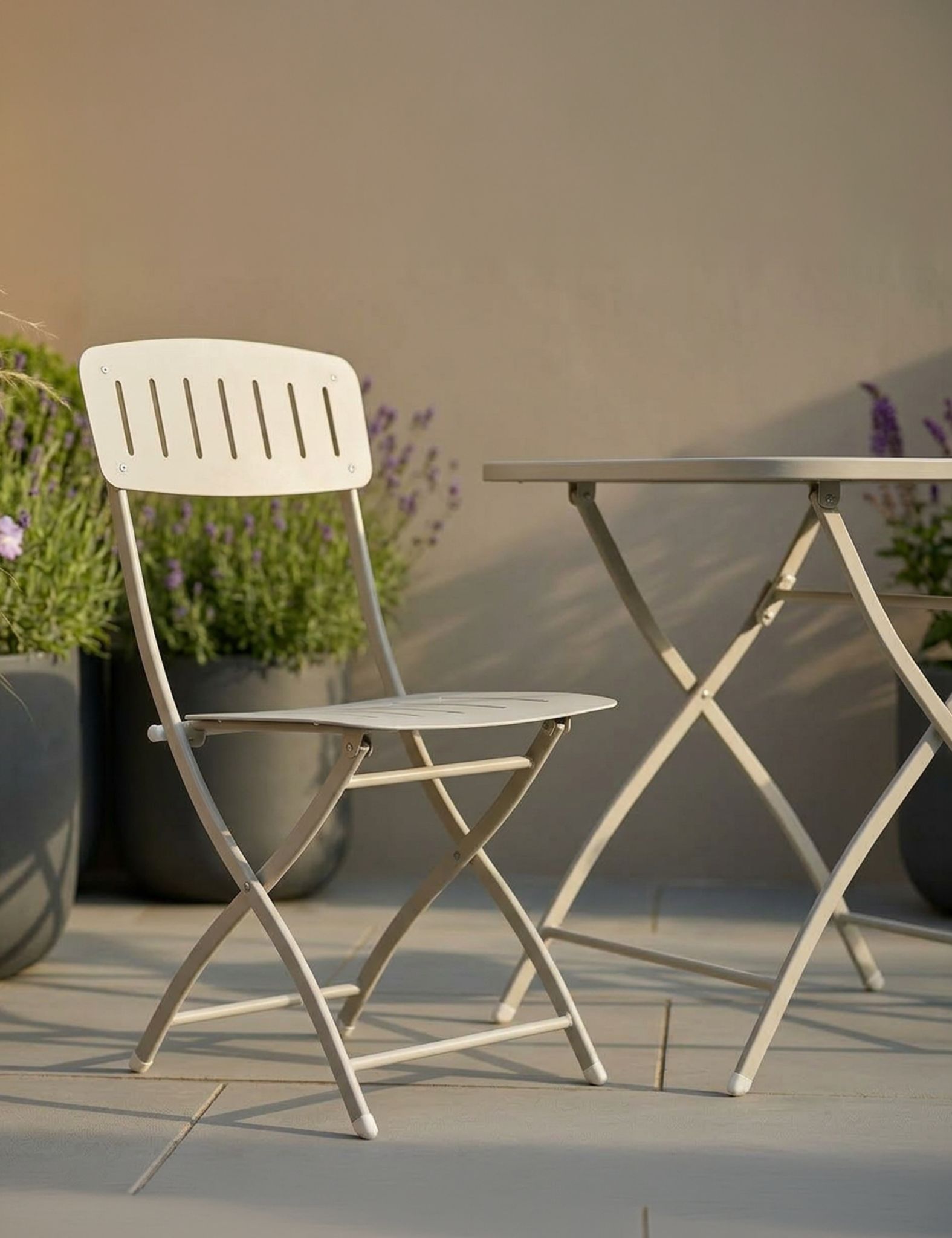 Image of White folding chair and table set on a patio with plants in the background