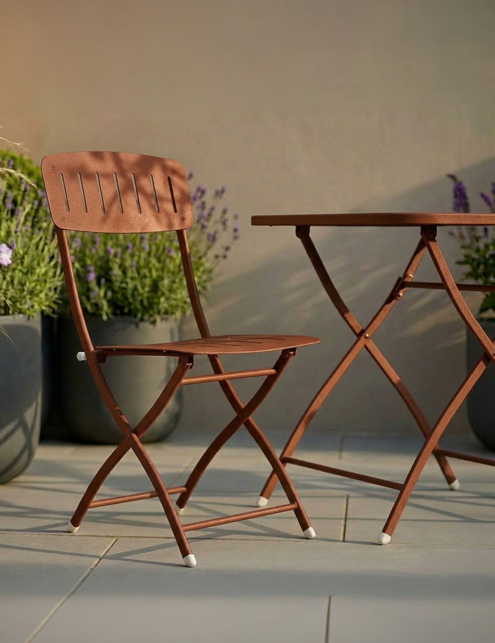 Image of Brown metal folding chair and table set on a patio with plants in the background