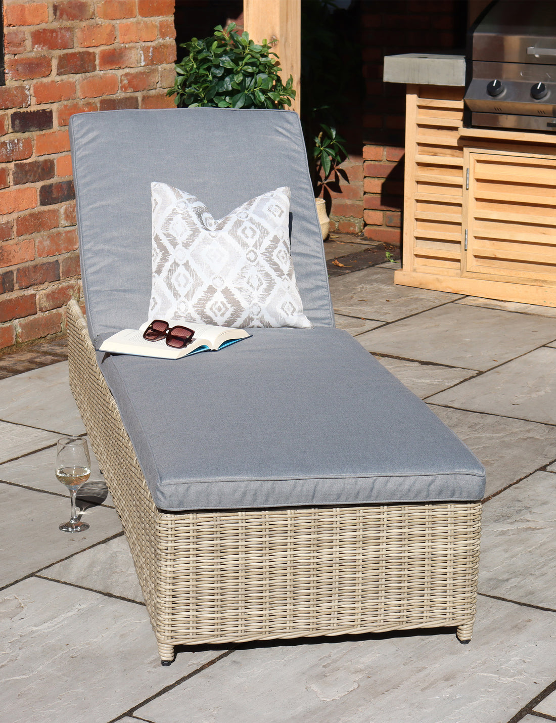 Rattan sun lounger with grey cushion and pillow on a stone patio