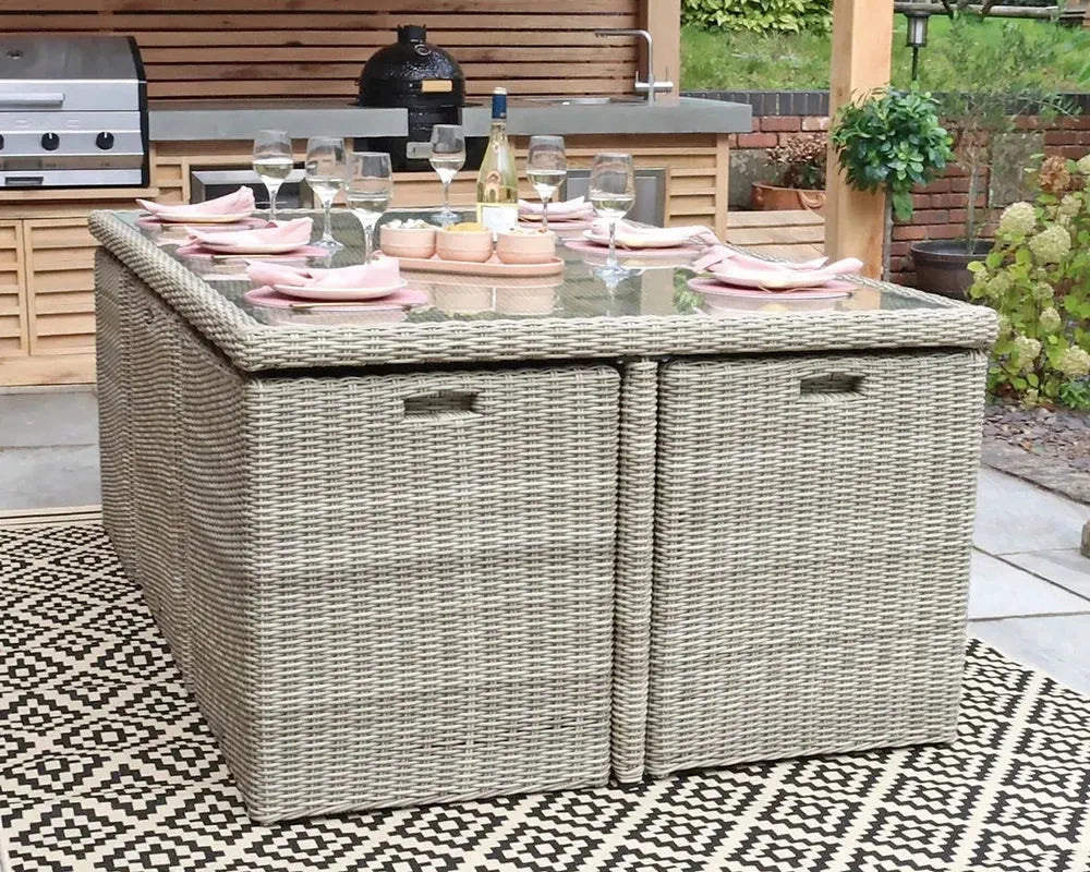 Image of Outdoor patio table with Rattan design on a patterned rug, surrounded by garden furniture and plants.