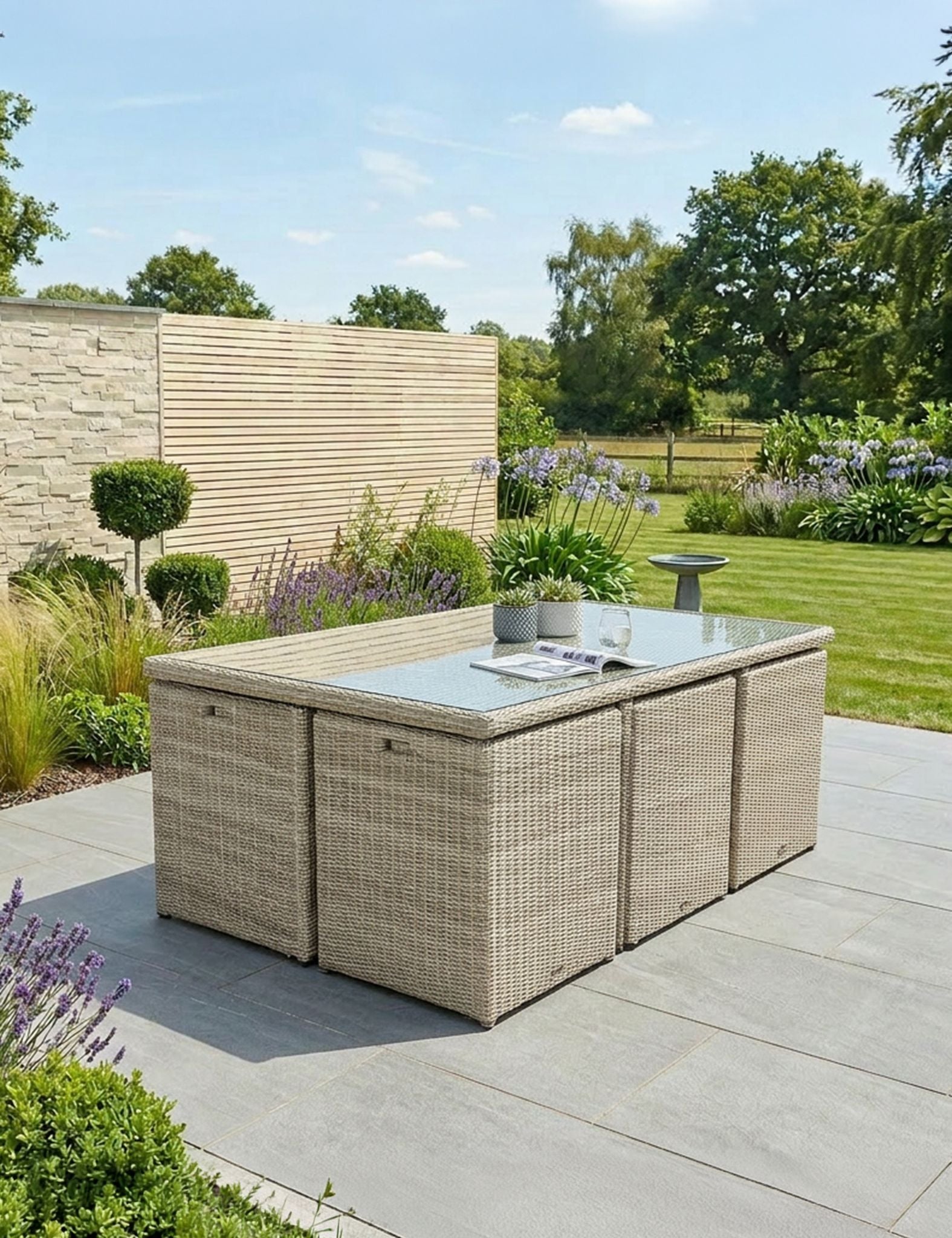 Image of Outdoor patio set with glass top table and storage boxes on a patio area with garden background.