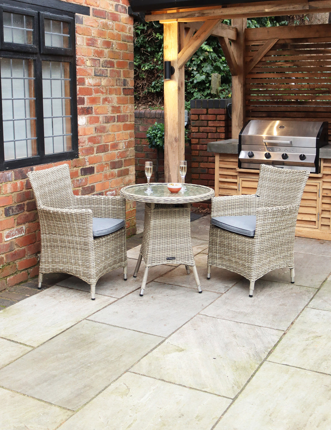 Rattan bistro set with round table and two grey cushioned chairs