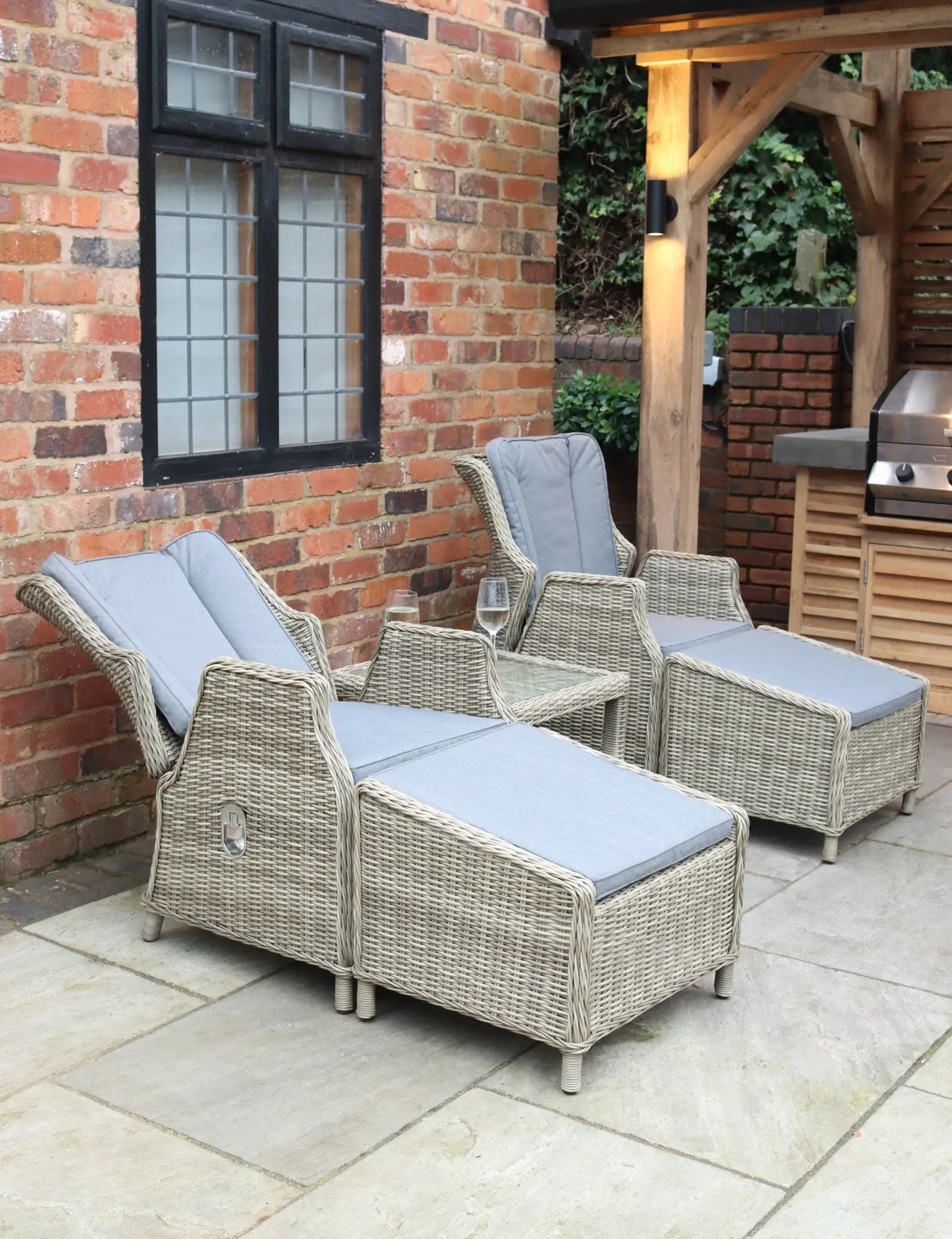 Two rattan recliner chairs with grey cushions and side table on patio
