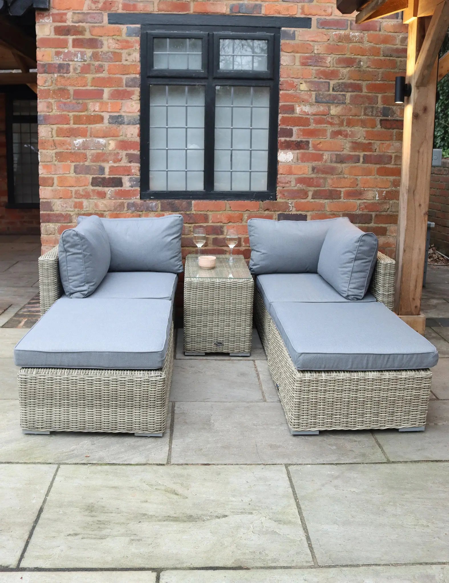 Image of Two wicker loungers with grey cushions and side table on a patio