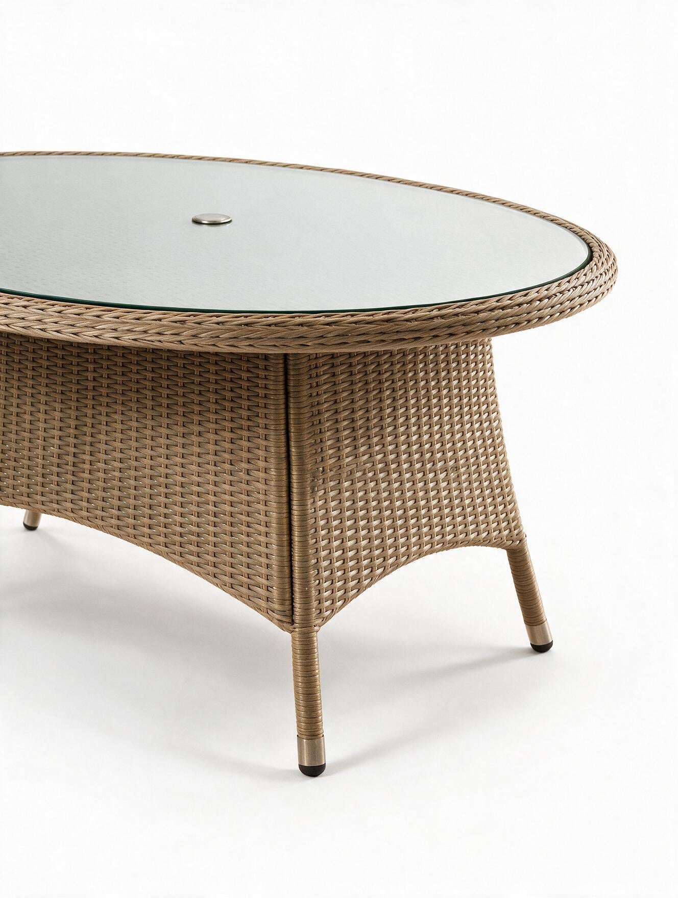 Image of An oval outdoor coffee table with a woven wicker frame in a light tan color and a clear glass top, shown against a plain white background.