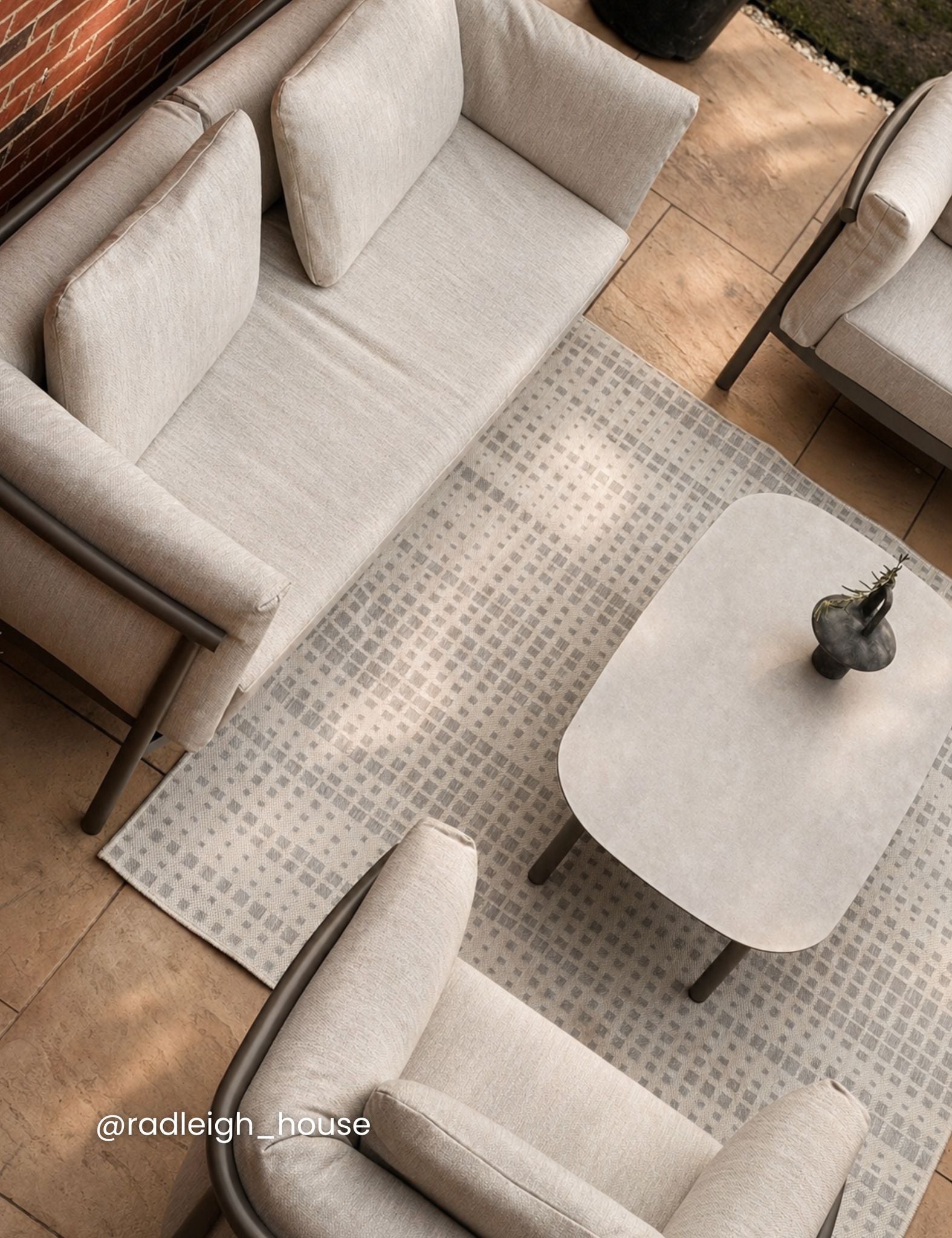 Image of Modern outdoor furniture set with beige sofa, coffee table, and rug on a wooden deck.